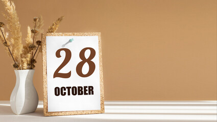october 28. 28th day of month, calendar date.White vase with dead wood next to cork board with numbers. White-beige background with striped shadow. Concept of day of year, time planner, autumn month