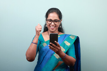 Portrait of a woman of Indian ethnicity looking at mobile phone with a cheering expression