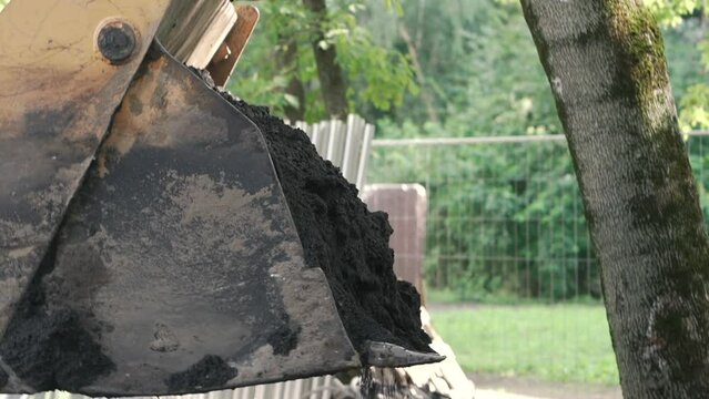 Bulldozer pouring out black soil from the laddle close up. Heavy machinery at work.