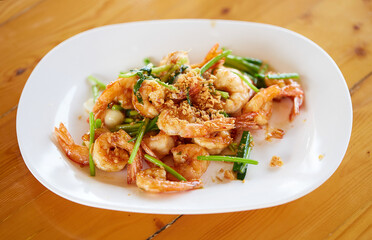 Fried shrimp with garlic and vegetables in white plate on wooden table, seafood. Top view.