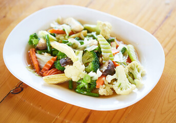 Stir Fried Mixed Vegetables (Sliced baby corn, oringi mushrooms, shiitake, carrots, kale, cauliflower, cauliflower and yard long beans) are served with white plate on wooden table. good healthy food
