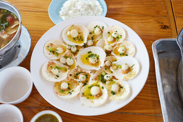 Butter-baked scallops on top with onions and spring onions place on wooden table.