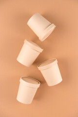 Eco kraft paper food containers for soup or hot beverages and food take away, cups with paper cap over light brown background, mockup image. Sustainable food packaging concept. Vertical image