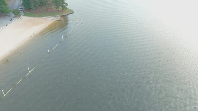 aerial footage of the rippling green waters of Lake Acworth surrounded by lush green trees, grass and plants with a beach on the banks of the lake at Proctor Landing Park at Lake Acworth in Acworth 