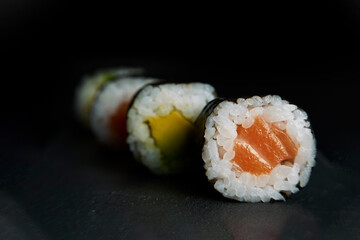 Sushi composition with salmon, avocado and cucumber. Sushi roll on a black background.