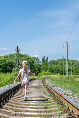 Rear view of little girl walking on railroad track against clear blue sky