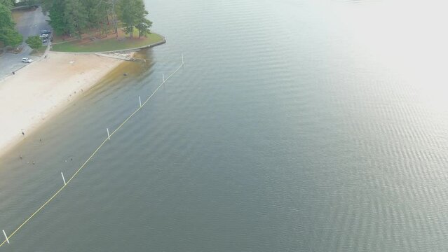 aerial footage of the rippling green waters of Lake Acworth surrounded by lush green trees, grass and plants with a beach on the banks of the lake at Proctor Landing Park at Lake Acworth in Acworth 