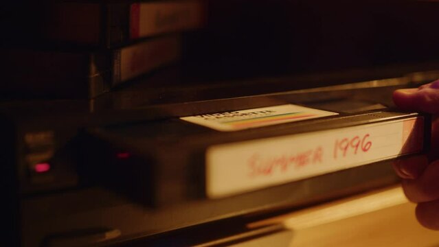 Close Up of a Person Inserting a VHS Cassette in a Player with Nostalgic Summer Footage from Home Video Camera. Retro Nineties Technology Concept. Old VCR Shot with Shallow Depth of Field and Bokeh.