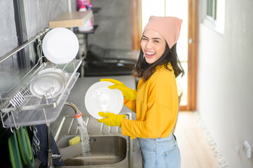 Young happy woman wearing yellow gloves washing dishes in kitchen at home