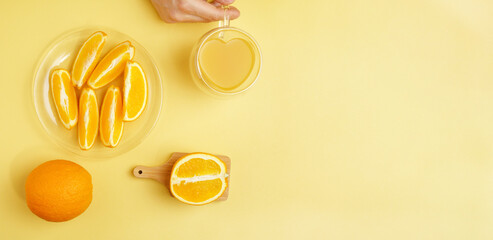 Glasses of fresh juice, fruit squeezer and ripe fresh oranges on yellow table top. Copy space