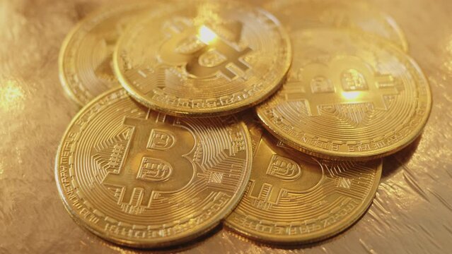 A heap of gold bitcoin coins, obverse with the iconic logo of the worlds leading cryptocurrency, rotating on a golden background, macro shot.