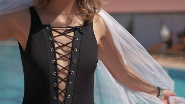 Closeups and details of young woman wearing black swimsuite and transparent cape. Filmed near outdoor swimming pool, slow motion