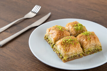 Pistachio baklava in a white plate on wooden background
