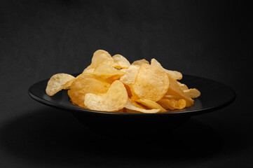 close-up of a pile of chips lying in a black plate standing on a black background
