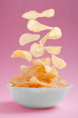 flying chips fall into a white plate standing on a pink background