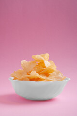 a pile of chips lies in a white plate standing on a pink background