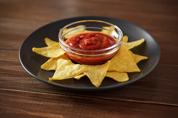 Nachos with tomato salsa on gray plate, on brown wooden table top, selective focus.