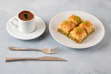 Pistachio baklava on a white plate with Turkish coffee.Traditional Turkish baklava and t coffee on a white background
