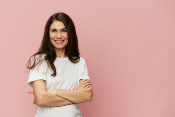 Obraz premium portrait of a cute, attractive woman on a pink background in a clean white t-shirt smiling pleasantly at the camera and folding her arms on her chest