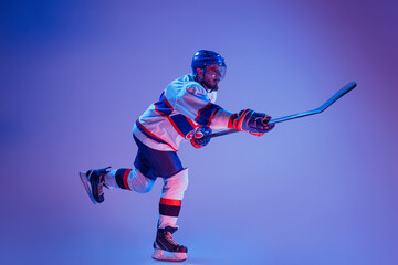 In action. Professional hockey player in sports uniform and protective equipment skating isolated on purple background. Concept of sport, active lifestyle, motion, movement, ad.