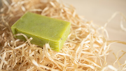 a piece of green soap lies on wrapping paper, on a wooden table surface. Hygiene, soap production,...