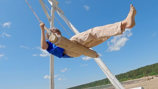 The guy at the sea going on the swings. Scenic view of happy boy on swing above the sea. Amusement park dream concept. Attention part of the hair is dyed blue.