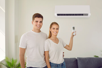 Portrait of a happy smiling couple using a modern air conditioner at home. Young husband and wife...