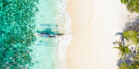 View from above, stunning aerial view of a Bangka boat in front of a white sand beach bathed by a turquoise water. Coron Island, Palawan, Philippines.