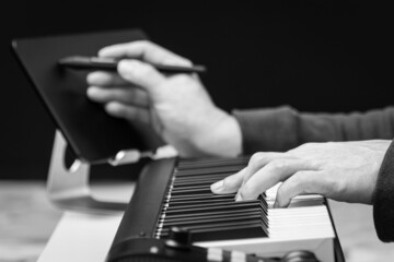 Fototapeta na wymiar close up black and white male songwriter hands writing a hit song with midi keyboard. songwriting concept