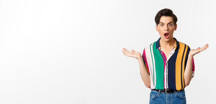 Image of surprised young male model staring at camera, spread hands sideways in complete disbelief, standing over white background