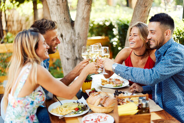 Group of young happy people toast with wine at lunch in restaurant during a sunny summer day