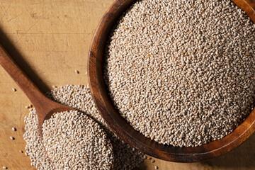 White chia seeds and wooden spoon in a wooden dish placed on a wooden background.