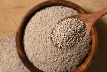 White chia seeds and wooden spoon in a wooden dish placed on a wooden background.