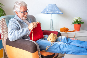 Portrait of relaxed senior man knitting at home sitting on the armchair. Knitting hobby activity and male caucasian people learning a new job