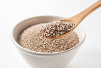 White chia seeds in a white bowl set against a white background. Scooping with a wooden spoon.