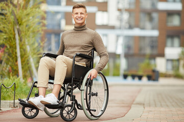 Portrait of cheerful excited handsome young handicapped man sitting in wheelchair outdoors