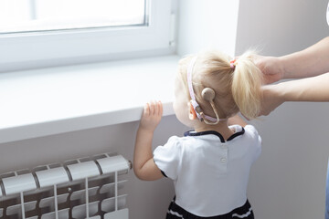 Mother fixing her daughter's cochlear implant hearing aid - deafness and diversity concept. Innovative technologies in treatment of deafness