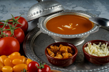 Bowl with tomato soup and ingredients, tomata soup in a metal bowl served with cheeese and croutons and different color of fresh  tomatoes