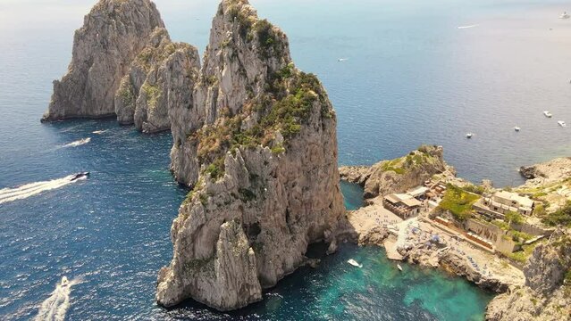 Aerial drone view of the Tyrrhenian sea coast of Capri, Italy. Rocky cliffs, blue water, floating boats, greenery