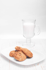 oatmeal cookies in a white rectangular plate and a glass mug with milk on a white wooden background