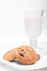 oatmeal cookies in a plate close-up and a glass mug with milk on a white wooden background