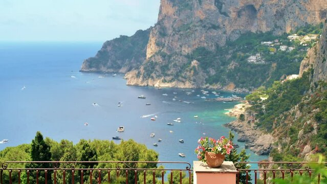 Tyrrhenian sea coast of Capri, Italy. Rocky cliffs, blue water, multiple floating boats, greenery