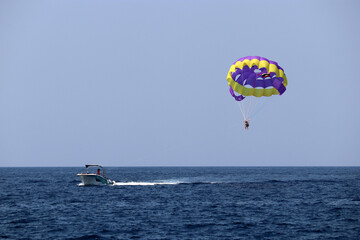 Fototapeta na wymiar Parasailing on the sea, speed boat and couple on parachute in blue sky. Beach vacation, extreme water sports