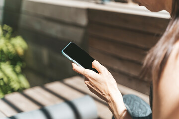 Sports girl using smartphone after yoga workout outdoors. Sports app, internet, technology, lifestyle concept.