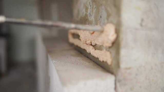 Contractor applies polyurethane foam adhesive with a gun nozle on concrete wall to glue autoclaved aerated concrete brick. Worker sprays the PU foam. Isolated view.
