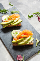 Two open sanwiches with dark rye bread, avocado, smoked salmon and radish