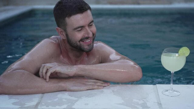 Hombre feliz  nadando en piscina con bebida