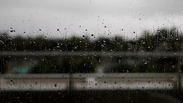 Rain drops rolling down a window on a hotel balcony, on a cloudy rainy bad wether day filmed in high quality 8k quality