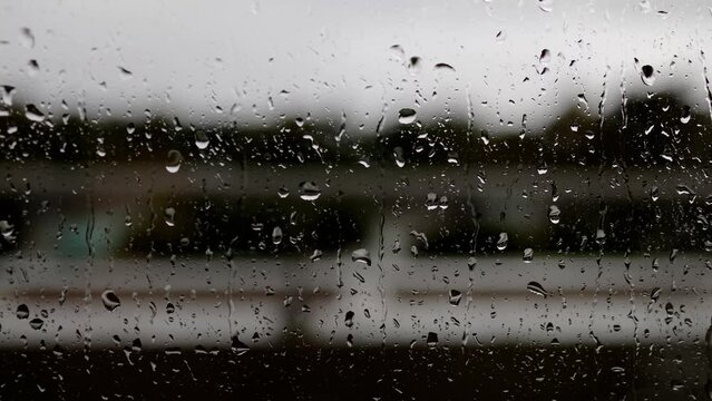 Rain drops rolling down a window on a hotel balcony, on a cloudy rainy bad wether day filmed in high quality 8k quality