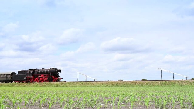 Old steam locomotive pulling railroad passenger cars in the countryside. 